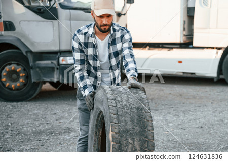 Moving the broken tire. Young truck driver is with his vehicle at daytime 124631836