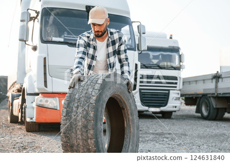 Moving the broken tire. Young truck driver is with his vehicle at daytime 124631840
