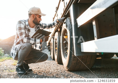 Working with wheels. Young truck driver is with his vehicle at daytime Working with wheels. Young truck driver is with his vehicle at daytime 124631859