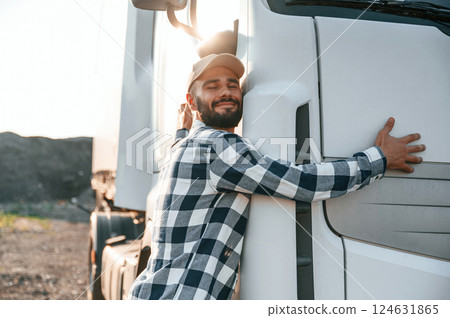 Embracing his vehicle. Young truck driver is outdoors at day time Embracing his vehicle. Young truck driver is outdoors at day time 124631865