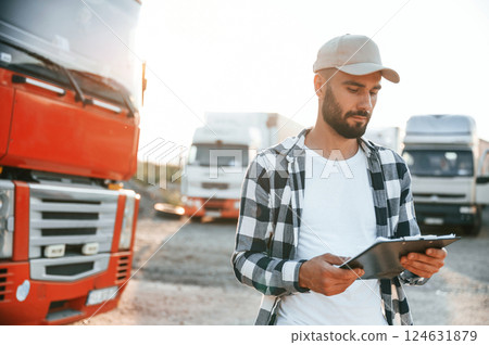 Looking at document in notepad. Young truck driver is with his vehicle at daytime 124631879
