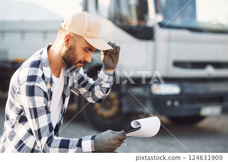 Sitting and reading the document. Young truck driver is with his vehicle at daytime Sitting and reading the document. Young truck driver is with his vehicle at daytime 124631909