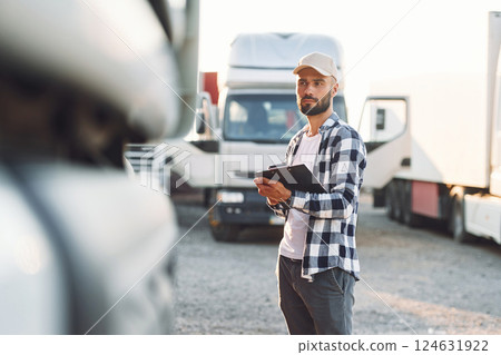With black notepad. Young truck driver is with his vehicle at daytime With black notepad. Young truck driver is with his vehicle at daytime 124631922