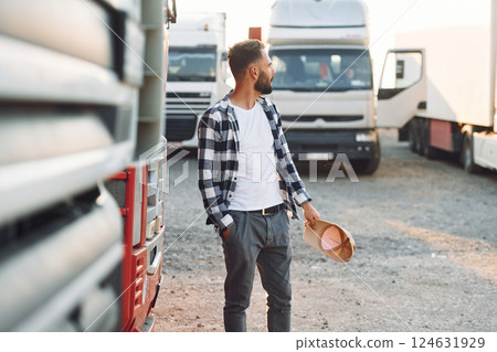 Standing and feeling bored. Young truck driver is with his vehicle at daytime Standing and feeling bored. Young truck driver is with his vehicle at daytime 124631929