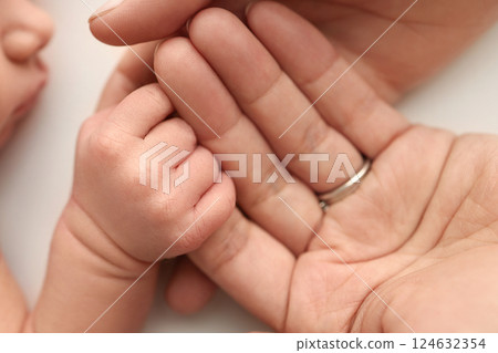 Close-up little hand of child and palm of mother and father. The newborn baby has a firm grip on the parent's finger after birth. A newborn holds on to mom's, dad's finger.  124632354