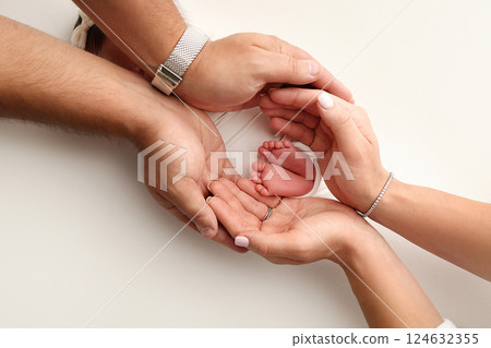 A father and mother hold the feet of a newborn child in a white blanket on a white background.. The feet of a newborn in the hands of parents. Photo of foot, heels and toes.The palms of the parents. A father and mother hold the feet of a newborn child in a white blanket on a white background.. The feet of a newborn in the hands of parents. Photo of foot, heels and toes.The palms of the parents. 124632355