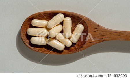 Vitamin capsules scattered on a wooden spoon.  124632993