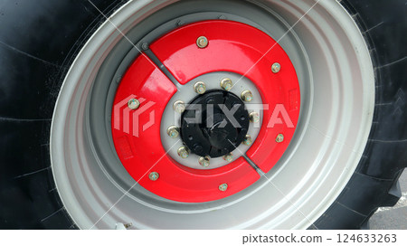 Detailed close up of a big tractor wheel showcasing vibrant red hub and metal bolts on outer rim 124633263