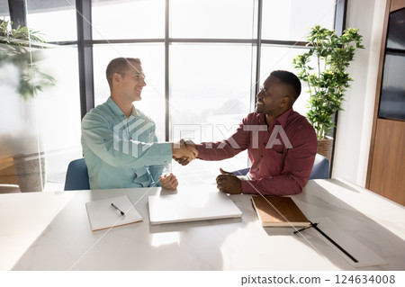 Two multinational business partners shaking hands in boardroom 124634008