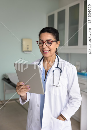 Positive experienced middle aged doctor woman using tablet for communication 124634069
