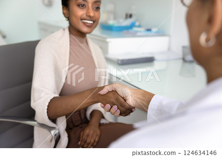 Positive young Black patient shaking hands with Caucasian doctor woman Positive young Black patient shaking hands with Caucasian doctor woman 124634146