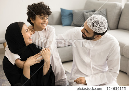 Muslim couple with little 7s son cuddling seated on floor 124634155