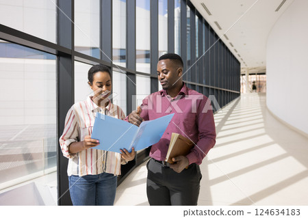 Colleagues standing in hallway leading professional conversation regarding joint task 124634183