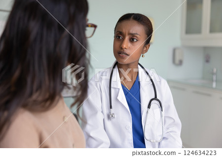 Serious young Black doctor listening to patient on checkup meeting 124634223