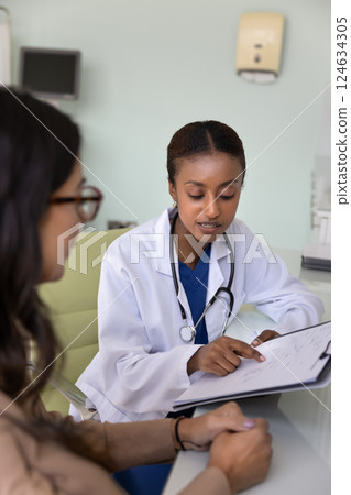 Serious Black practitioner showing medical records to mature Caucasian patient 124634305