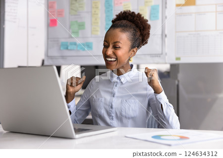 Happy excited young Black businesswoman winning prize at laptop 124634312