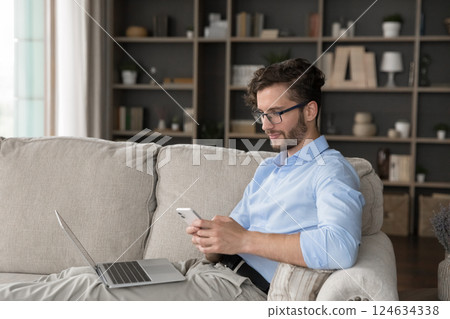 Relaxed millennial male spending time on cozy couch using gadgets 124634338