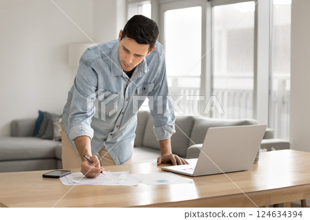Man leaning over desk, making notes, focused on paperwork Man leaning over desk, making notes, focused on paperwork 124634394