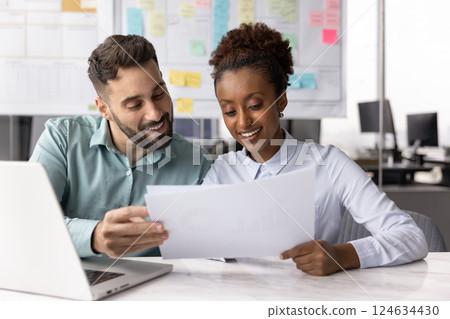 Couple of positive multiethnic business colleagues analyzing paper financial report Couple of positive multiethnic business colleagues analyzing paper financial report 124634430