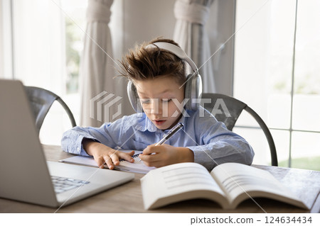 Boy listens audio course, e-learning seated at table with laptop 124634434