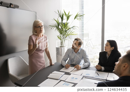 Serious middle-aged businesswoman holds business meeting with shareholders Serious middle-aged businesswoman holds business meeting with shareholders 124634435