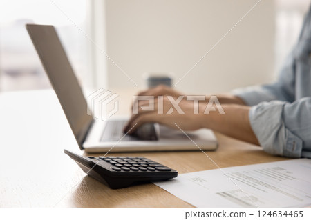 Man typing on laptop seated at table with calculator, closeup 124634465