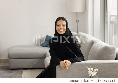 Middle Eastern woman dressed in traditional abaya resting on sofa 124634541