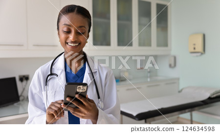 Cheerful young Black physician woman typing on mobile phone 124634598