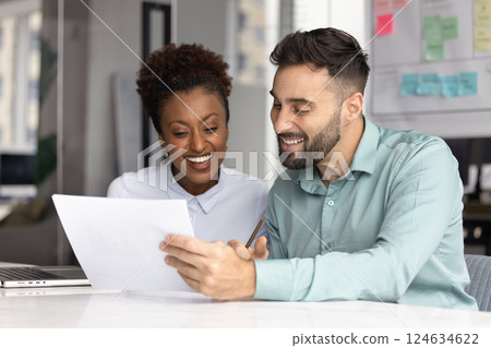 Cheerful young African and Caucasian managers reading paper document Cheerful young African and Caucasian managers reading paper document 124634622