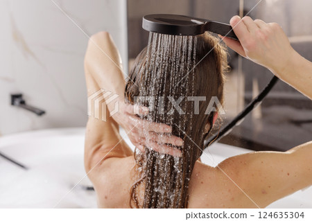 Woman rinsing hair under shower in bathtub, luxury spa haircare and beauty routine at home, wellness relaxation concept in modern bathroom interior. Woman rinsing hair under shower in bathtub, luxury spa haircare and beauty routine at home, wellness relaxation concept in modern bathroom interior. 124635304