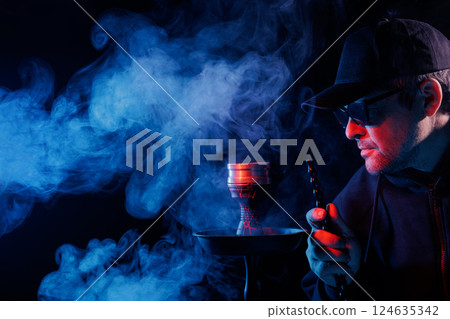 Man smoking hookah, adjusting hot charcoal with tongs in a smoky, moody atmosphere, illuminated by red and blue lighting, Man smoking hookah, adjusting hot charcoal with tongs in a smoky, moody atmosphere, illuminated by red and blue lighting, 124635342