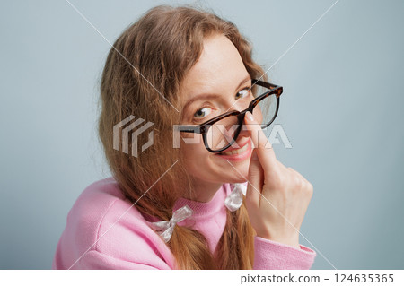 A woman with long hair and glasses playfully adjusts her glasses, smiling at the camera. She is wearing a pink sweater, concept vision problem A woman with long hair and glasses playfully adjusts her glasses, smiling at the camera. She is wearing a pink sweater, concept vision problem 124635365