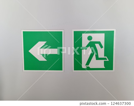 Two green signs indicating emergency exits. One shows a left arrow, the other a figure running towards an exit. 124637300