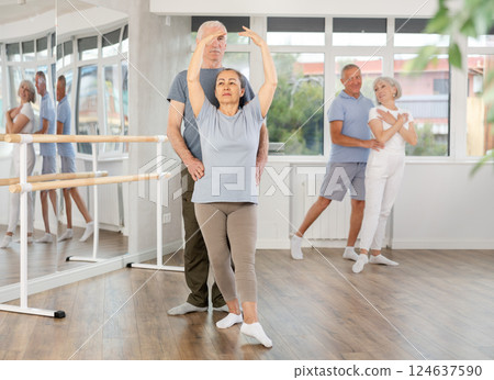 Elderly couple perform ballet pose with support during group training class in ballet hall Elderly couple perform ballet pose with support during group training class in ballet hall 124637590