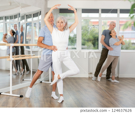 Elderly couple perform ballet pose with support during group training class in ballet hall Elderly couple perform ballet pose with support during group training class in ballet hall 124637626