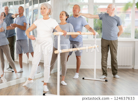 Diligent mature men and women practicing basic positions with trainer standing by ballet 124637633