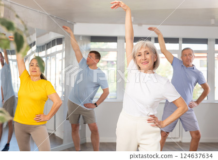 Elderly woman practicing Tai Chi with group in training room Elderly woman practicing Tai Chi with group in training room 124637634