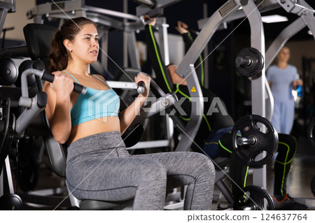 Sporty young woman using arm extension machine in gym Sporty young woman using arm extension machine in gym 124637764