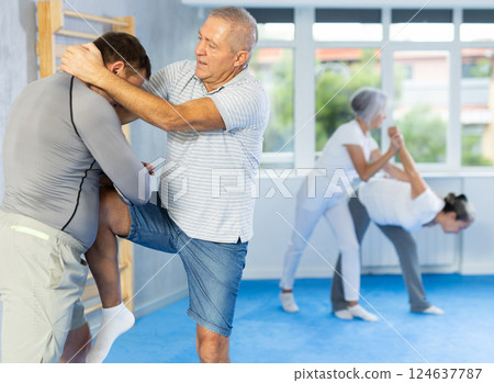 Senior man in pair with middle-aged coach train Krav Maga and self-defense skills. 124637787