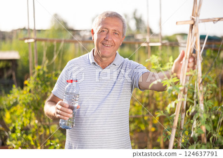Senior man stands near garden bed and drinks water from bottle 124637791