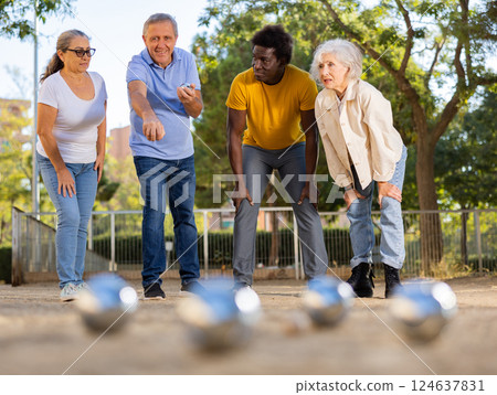 Mature casual diverse pensioners throwing petanque balls far away on a spring sunny day in the park 124637831