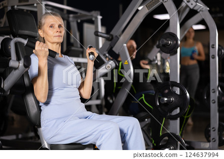 Sporty senior woman working out shoulders muscles on exercise machine 124637994
