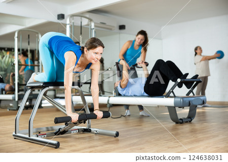 Middle-aged woman practicing pilates on pedal fitness chair in sports hall 124638031