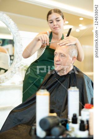 Young female hairdresser working with scissors and comb with mature man 124638042