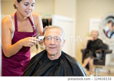 Senior client getting haircut with clipper from skilled female barber in barbershop 124638158