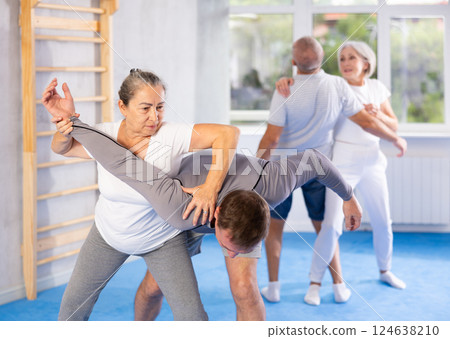 Senior woman in pair with middle-aged coach train Krav Maga and self-defense skills. Senior woman in pair with middle-aged coach train Krav Maga and self-defense skills. 124638210