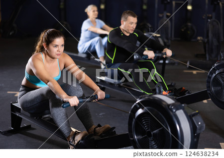 Athlete woman works on rowing simulator in gym 124638234