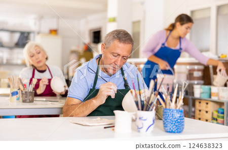 Mature craftsman painting clay plates acrylic paints in art studio 124638323