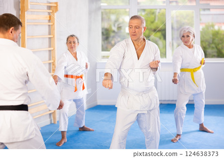 Group of elderly people in white kimonos learn to punch and kick under the guidance of trainer. Karate lessons 124638373