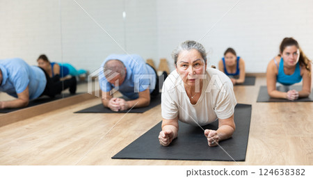 Elderly woman practicing pilates on mat in gym area Elderly woman practicing pilates on mat in gym area 124638382